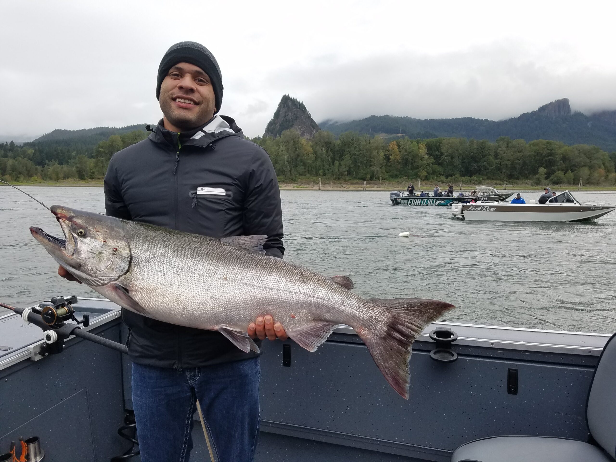 Guy holding large salmon in boat with Beacon Rock in background