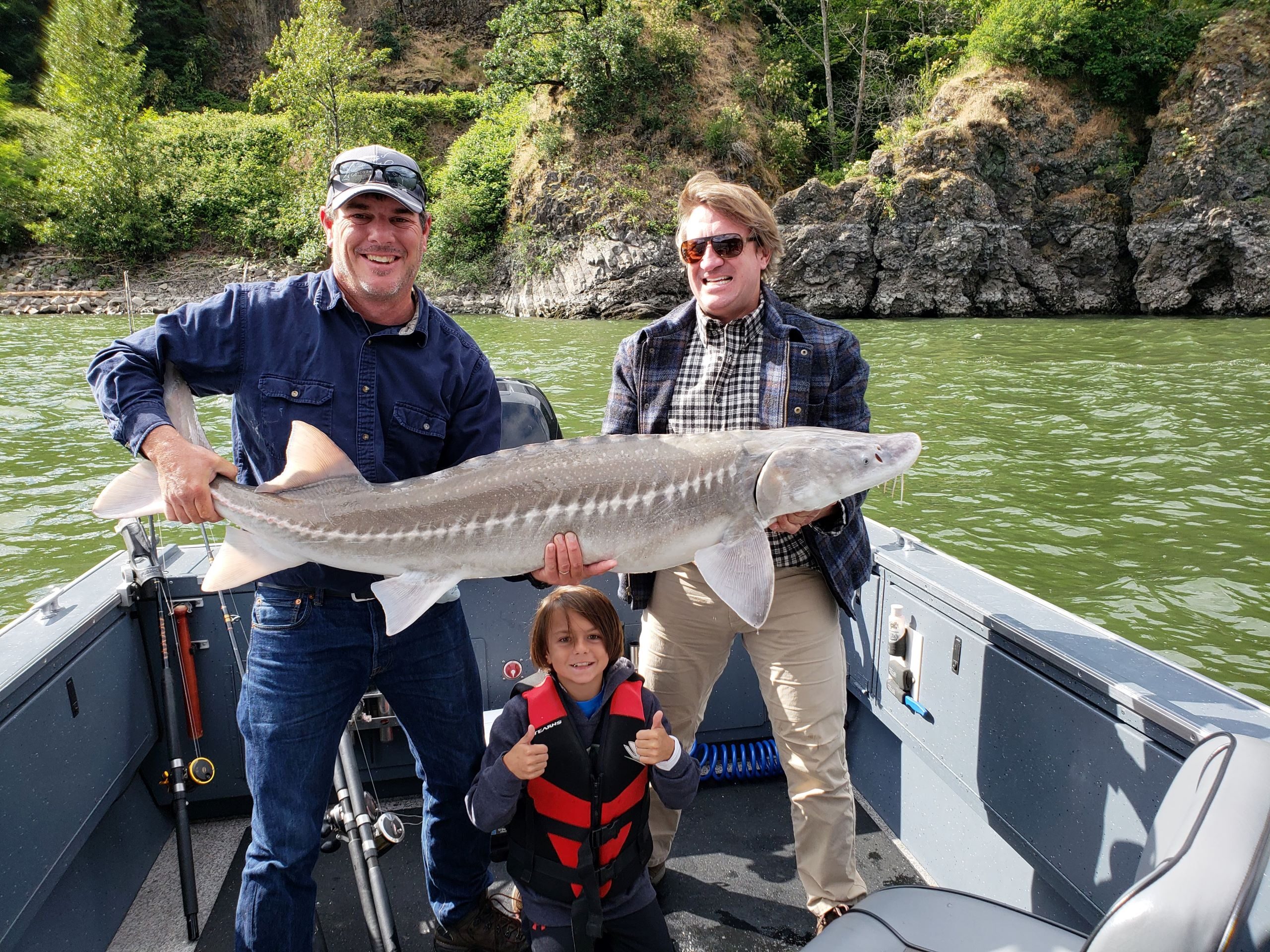 2 people holding sturgeon with little kid giving thumbs up