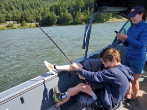2 boys reeling oversize Sturgeon using their whole body, and the boat
