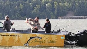 2 people in a yellow boat holding a sturgeon